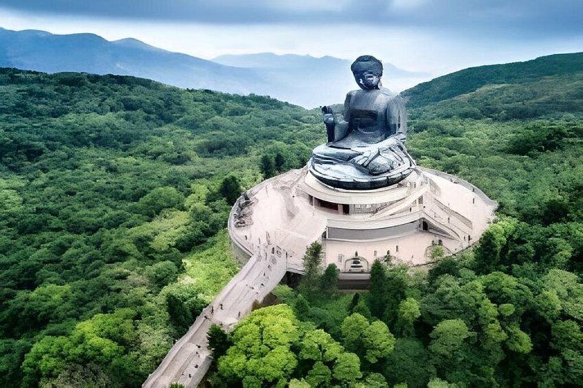 A large Buddha statue surrounded by lush greenery and mountains in the background. 1