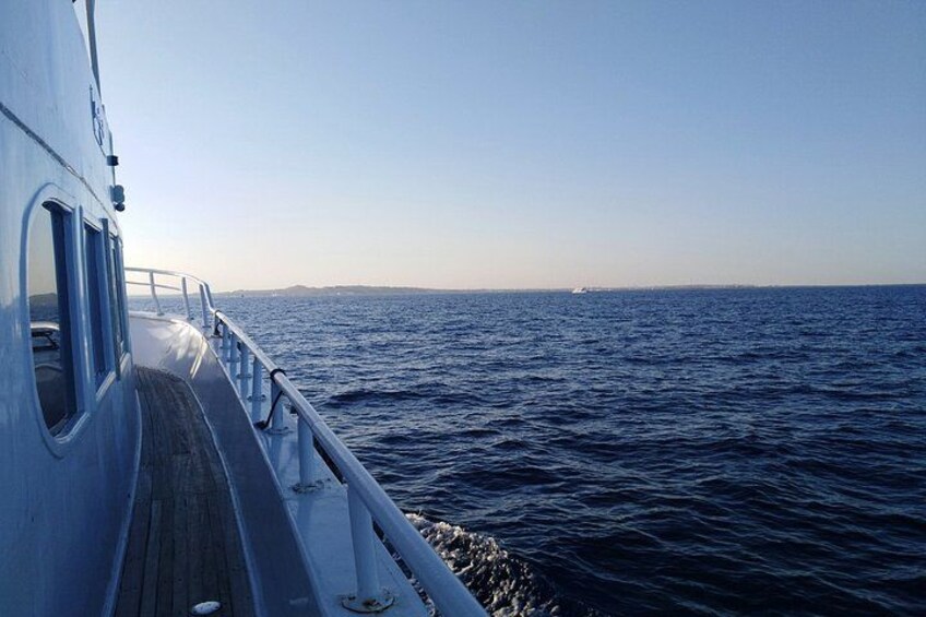 A boat deck with a railing, calm sea, and distant land. 3