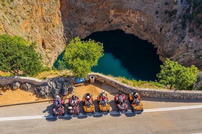 Un grupo de motociclistas en una carretera con un acantilado rocoso y un cuerpo de agua al fondo. 3
