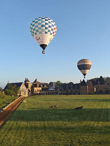 Two hot air balloons over a grassy field with historic buildings in the background. 5