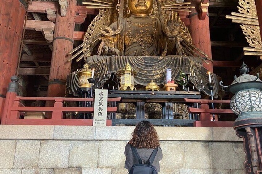 A large golden Buddha statue in a temple with a sign in front. 5