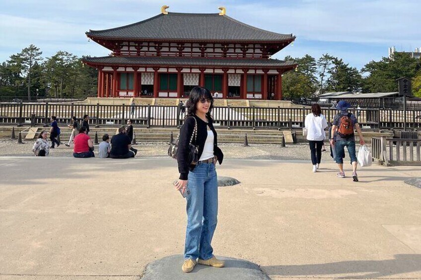 A traditional Japanese building with a tiled roof and red columns, surrounded by a stone walkway with people walking and sitting. 4