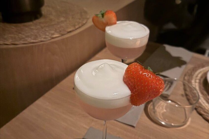 Two cocktails with a strawberry garnish on a wooden bar counter. 3