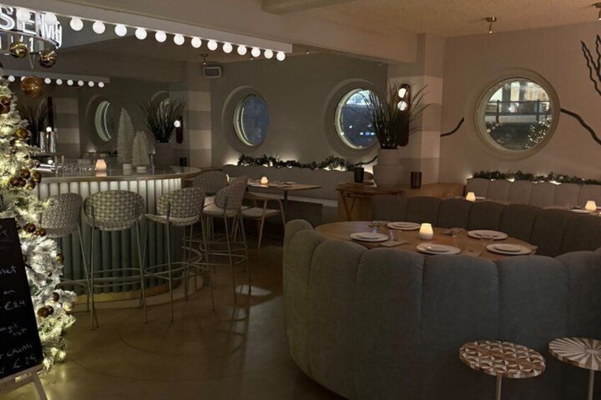 A cozy restaurant interior with round tables, bar stools, and a Christmas tree. 2