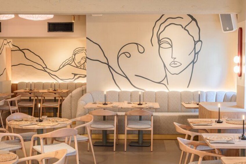 A restaurant interior with a modern design, featuring a large wall mural, cushioned seating, and round tables. 5