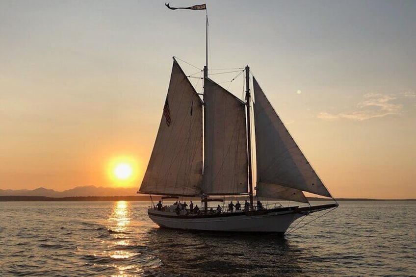 Un voilier avec plusieurs voiles naviguant sur une étendue d’eau calme au coucher du soleil. 2