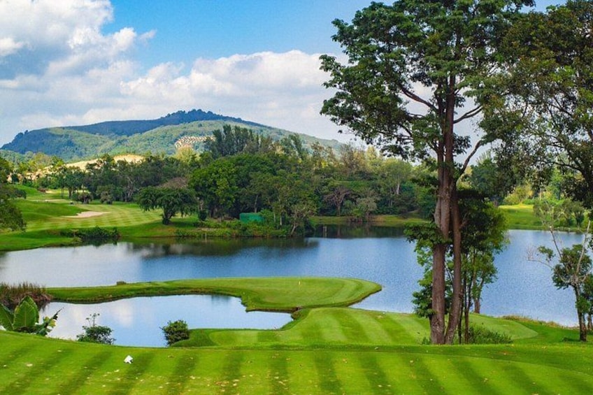 A golf course with a pond, trees, and a hilly landscape. 1