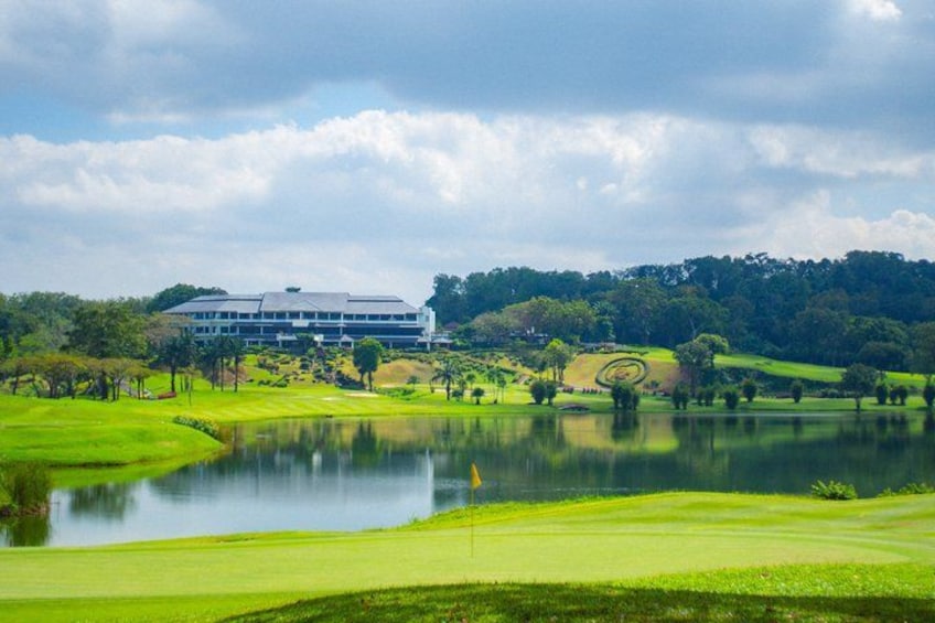 A golf course with a pond, a building, and a forested hill. 3