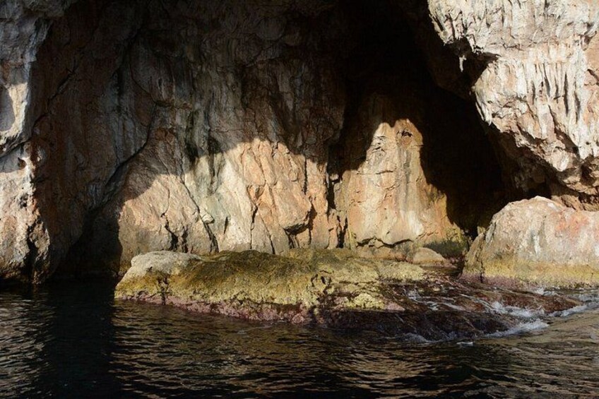 Entrada a una cueva con estalactitas y estalagmitas, agua que fluye por el interior y una repisa rocosa. 4