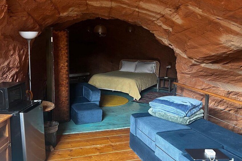 En grotta med en säng, en blå soffa och ett trägolv. 4