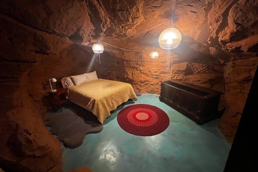 A cave-like room with a bed, a red rug, and two wall-mounted lamps. 2