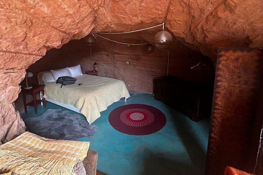 Una habitación tipo cueva con una cama, una mesita pequeña y una alfombra circular roja. 4
