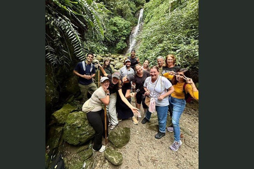 A group of people posing in a forested area with a waterfall in the background. 2