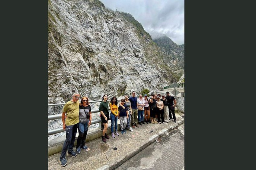 A group of people standing on a concrete ledge with a rocky mountain in the background. 3