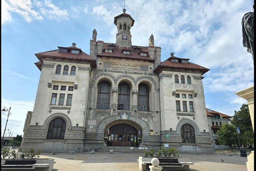 A historic building with a central arched entrance, a clock tower, and decorative stonework. 2
