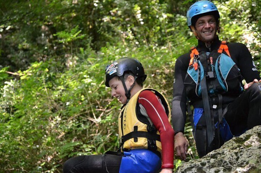 Two people sitting on a rock in a forested area, wearing helmets and safety gear. 4