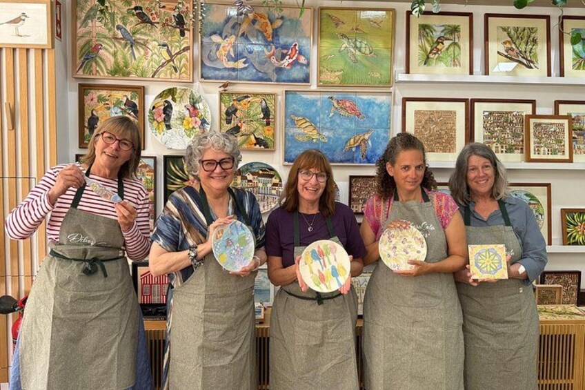 A group of people holding ceramic plates with various designs, standing in front of a wall with framed artwork. 2
