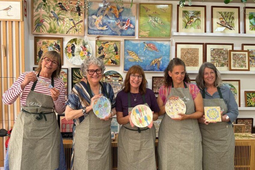 Five people holding circular objects with colorful patterns, standing in front of a wall with framed artwork. 2