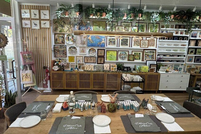 A dining area with a wooden table set for six, surrounded by framed artwork and potted plants. 1