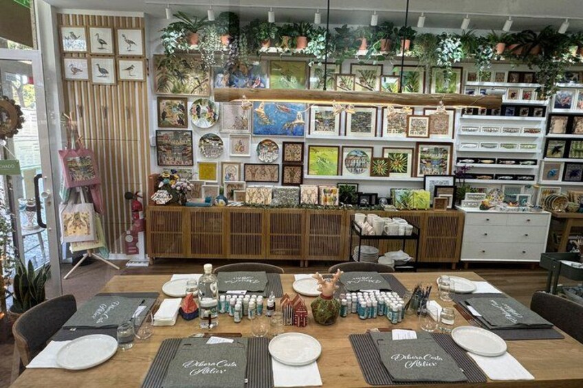 A dining area with a wooden table set for a meal, surrounded by shelves with framed artwork and plants. 1