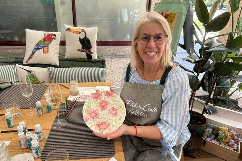A person holding a plate with a floral design, seated at a table with various items including bottles, a glass, and a placemat. 3