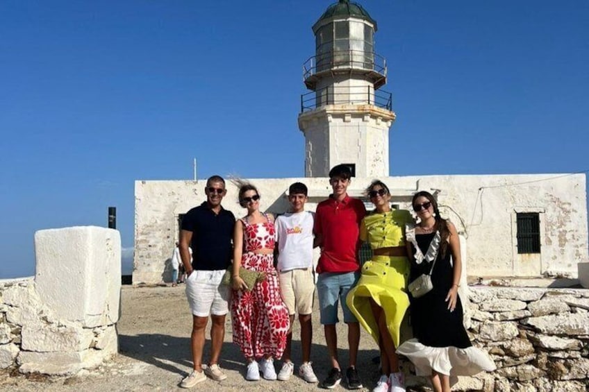 A group of people standing in front of a lighthouse and a white building. 1