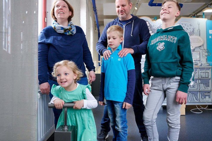 A group of people in a hallway with a child in a wheelchair, a child in a blue shirt, and a person in a green hoodie. 5
