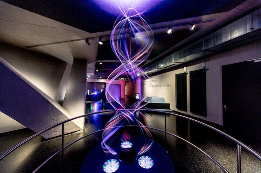 A modern indoor space with a curved railing, a spiral light installation, and a reflective floor. 4