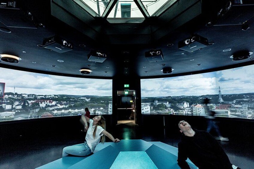 A room with a large window overlooking a cityscape, a staircase, and a person sitting on the floor. 1