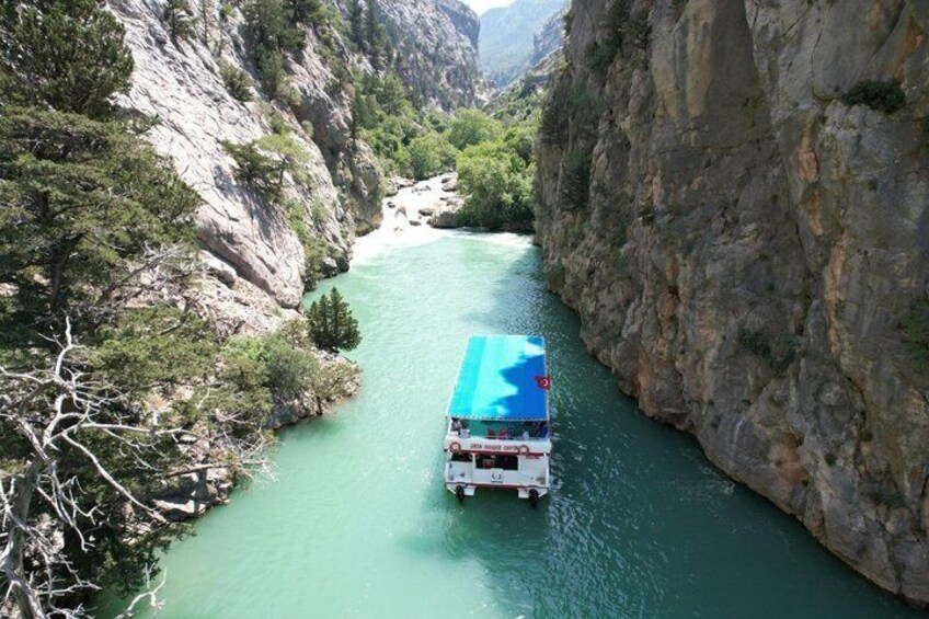 A boat with a blue and white canopy navigating a narrow river surrounded by rocky cliffs and greenery. 1
