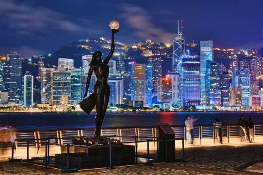 A nighttime cityscape with a statue of a woman holding a globe, a waterfront, and a bridge. 1
