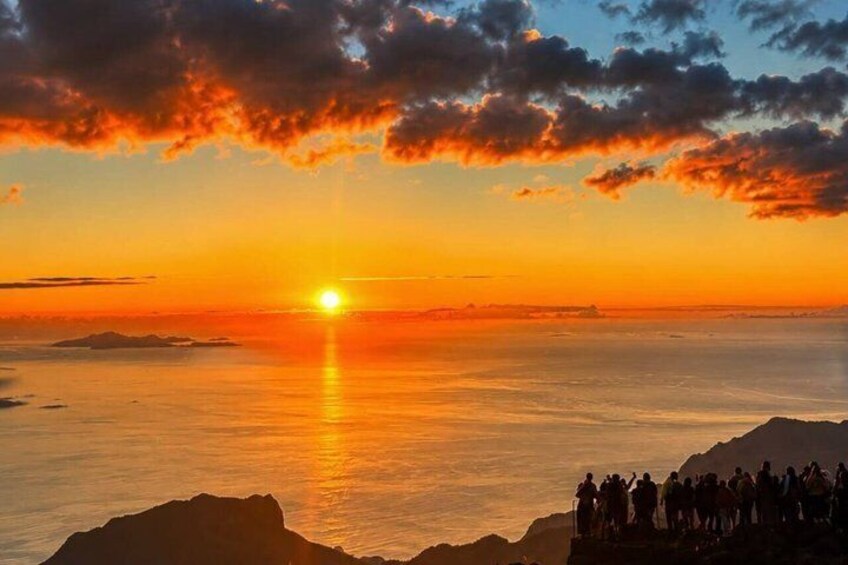 A sunset over a calm sea with a silhouette of people on a cliff. 2