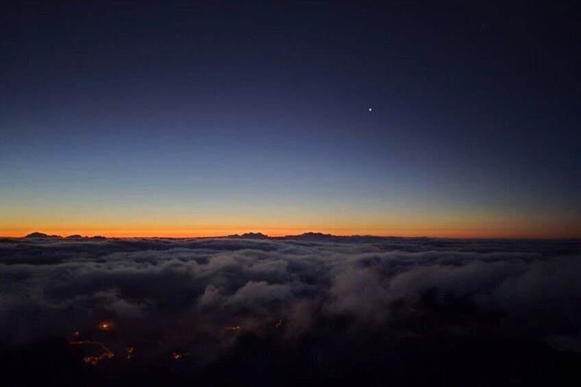 A night sky above a sea of clouds with a crescent moon visible. 1