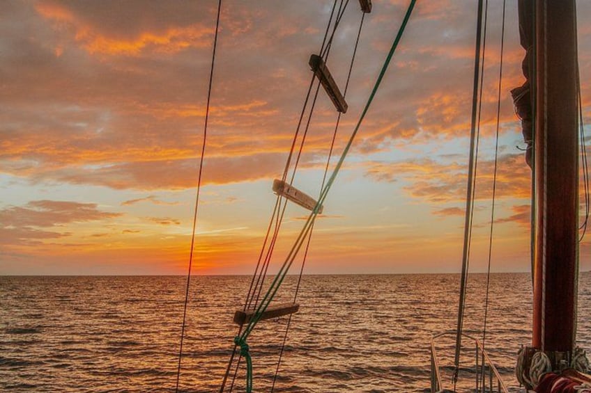 A sunset over the ocean with a sailboat's rigging and a wooden mast. 5