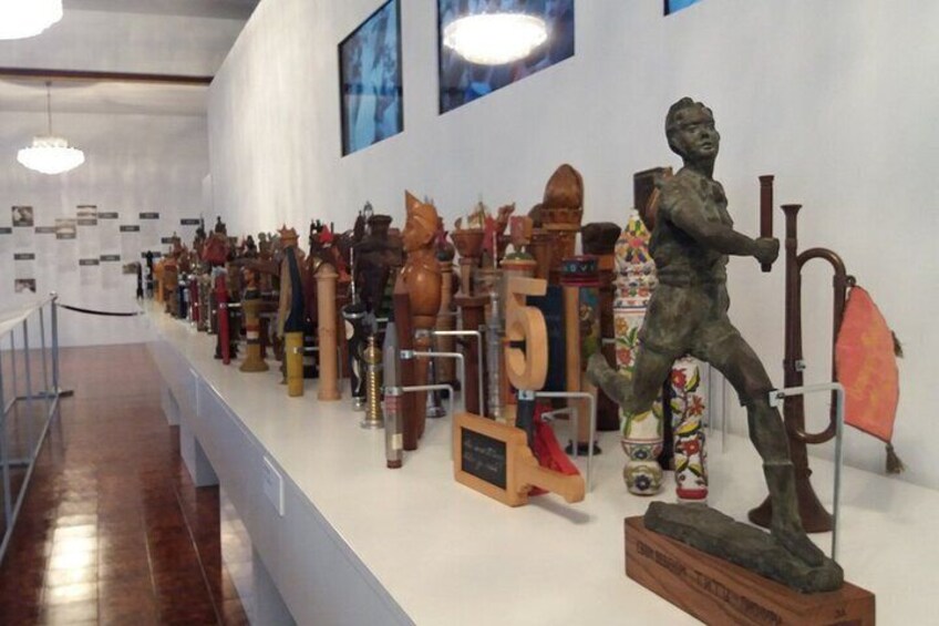 Een museumexpositie met diverse houten en metalen sculpturen, waaronder een opvallende bronzen statue van een figuur met een staf. 5