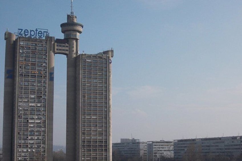 Twee hoge gebouwen, waarvan er een 'Zepler' op de gevel heeft, met een toren bovenop en een heldere lucht op de achtergrond. 2
