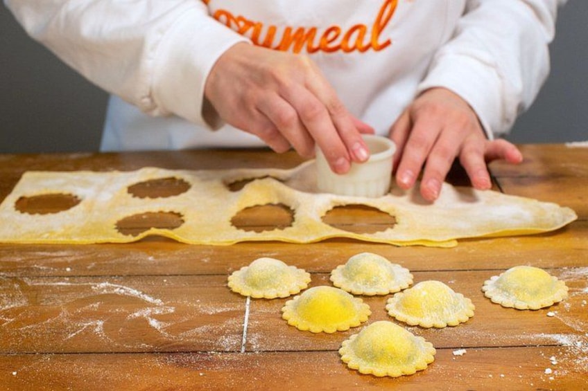 Hands shaping dough into ravioli on a wooden surface. 1