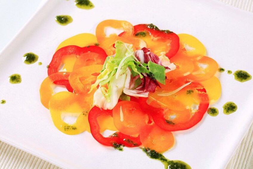 A white plate with a tomato salad, green sauce, and a small salad garnish. 4