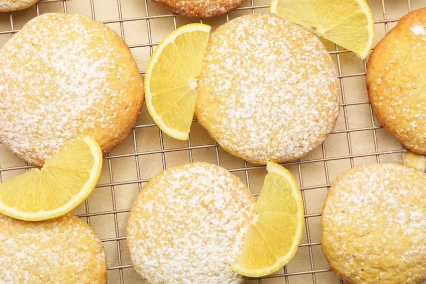 Round pastries dusted with powdered sugar and lemon slices on a cooling rack. 5