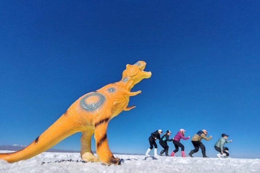 A large dinosaur statue, a clear blue sky, and a group of people running. 4
