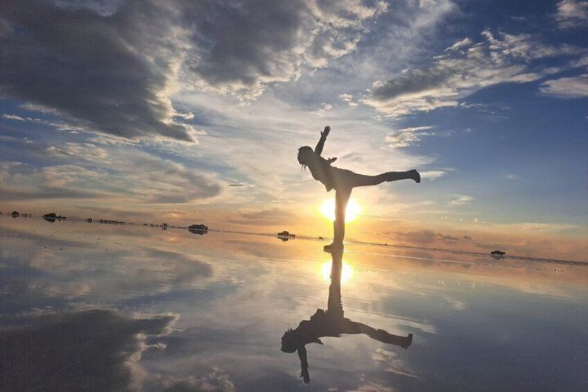 A person performing a balancing act on a reflective surface with the sun setting in the background. 1