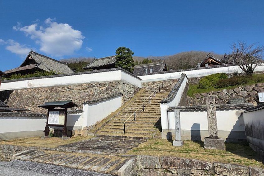 A traditional Korean stone staircase leading up to a temple complex with white walls and tiled roofs. 1