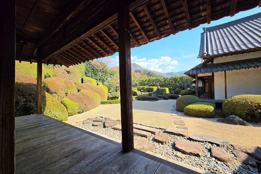 A traditional Japanese garden with a wooden walkway, stone lanterns, and a building with a tiled roof. 4