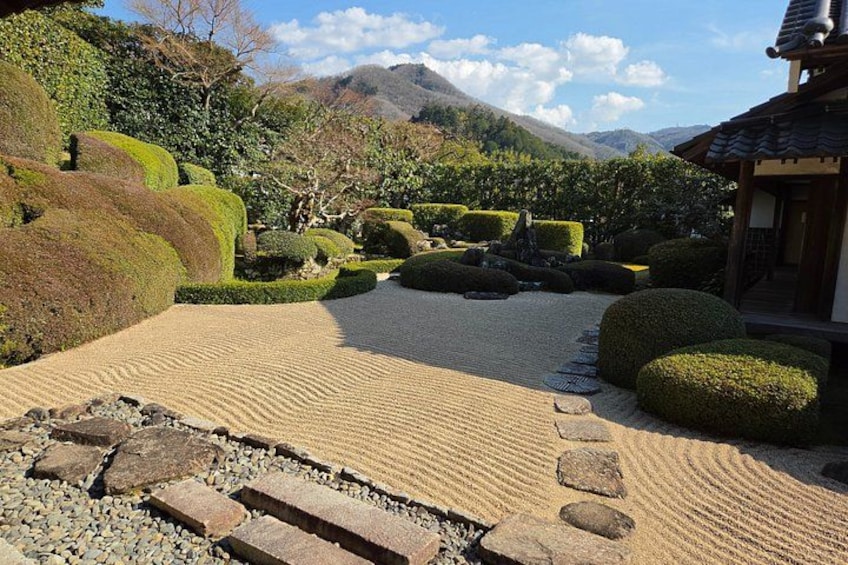 A traditional Japanese garden with a gravel path, stepping stones, neatly trimmed bushes, and a mountain in the background. 5