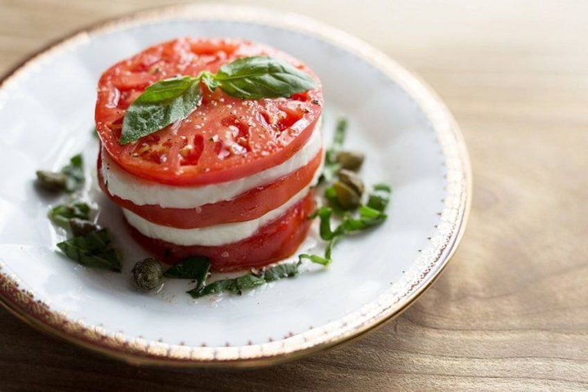 A layered tomato and mozzarella dish on a plate with basil leaves. 5