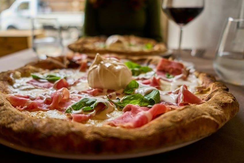 A pizza with toppings and a glass of red wine on a table. 3