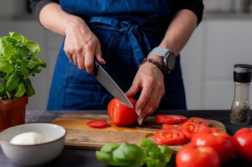 A person slicing a tomato on a wooden cutting board. 4