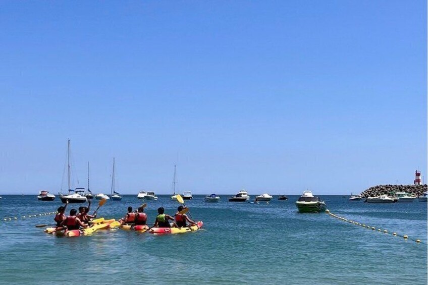 Un groupe de personnes pratiquant le kayak sur une étendue d’eau calme, avec plusieurs bateaux et un phare en arrière-plan. 5