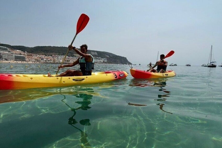 Deux personnes pratiquent le kayak sur une mer calme, avec une ville côtière en arrière-plan. 3