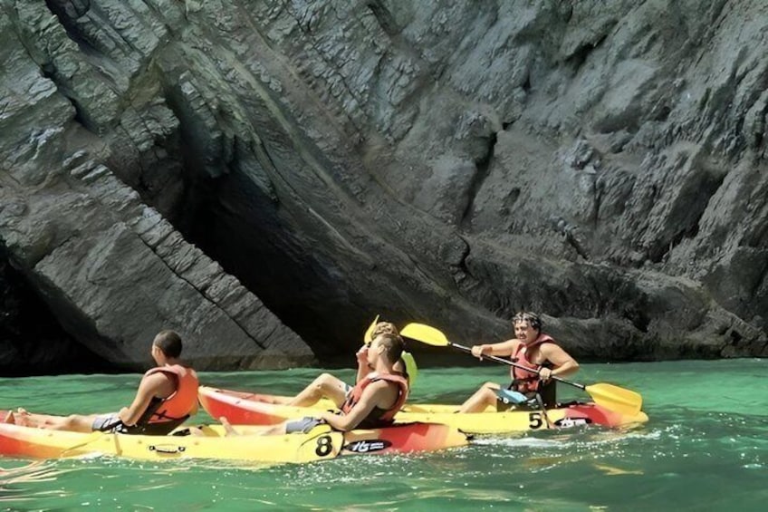 Trois personnes pratiquent le kayak sur une rivière paisible, avec une falaise rocheuse en arrière-plan. 1